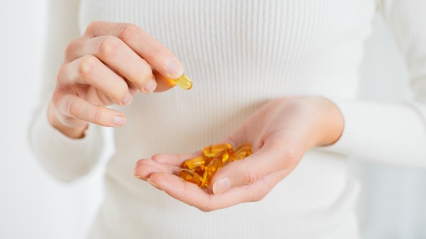 A close-up of a woman in a white shirting holding omega 3 capsules in her hand