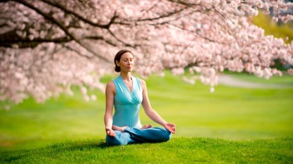 Woman practicing mindfulness for beginners by meditating in front of cherry blossom tree