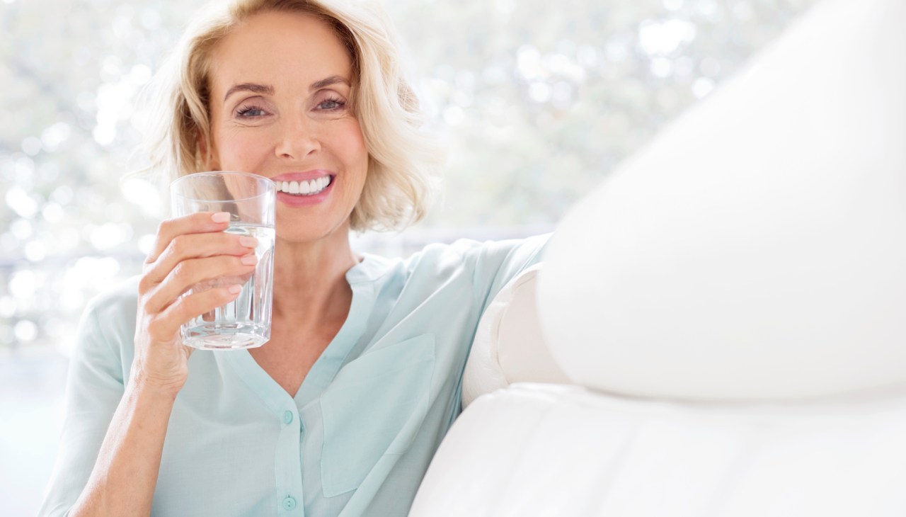 Mature woman smiling with glass of water.