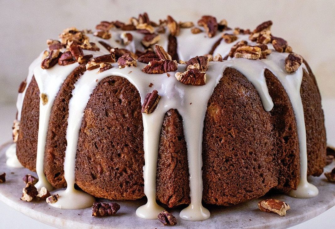 hummingbird bundt cake recipe on cake stand with frosting and nut topping