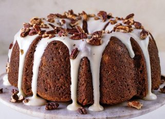 hummingbird bundt cake recipe on cake stand with frosting and nut topping