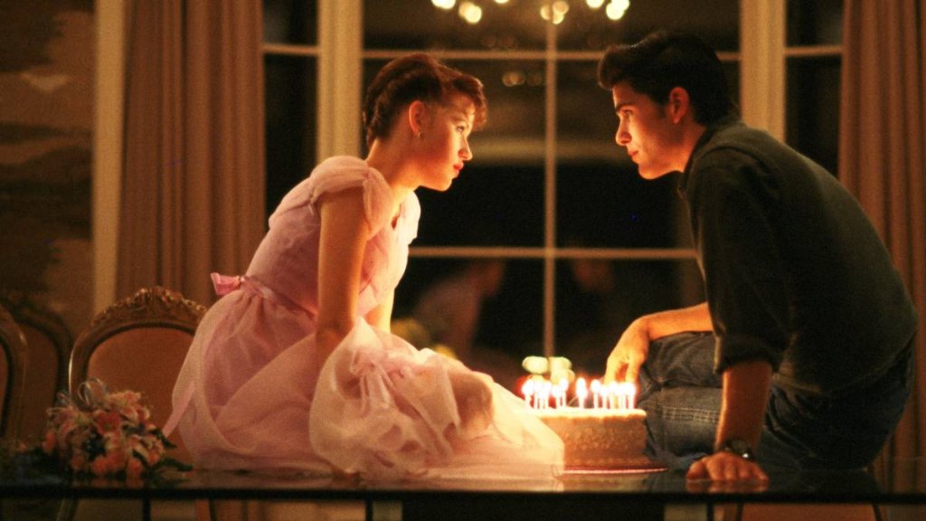 Girl and boy sitting on table in front of a cake