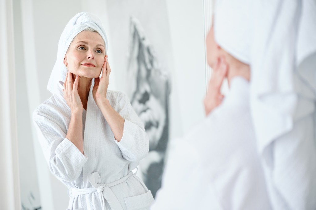 mature woman looking in mirror at smooth skin