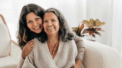 Daughter with her arms around her older mother, both smiling at the camera