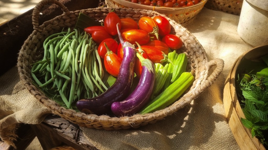 A basket filled with eggplant, tomatoes, greenbeans, and okra