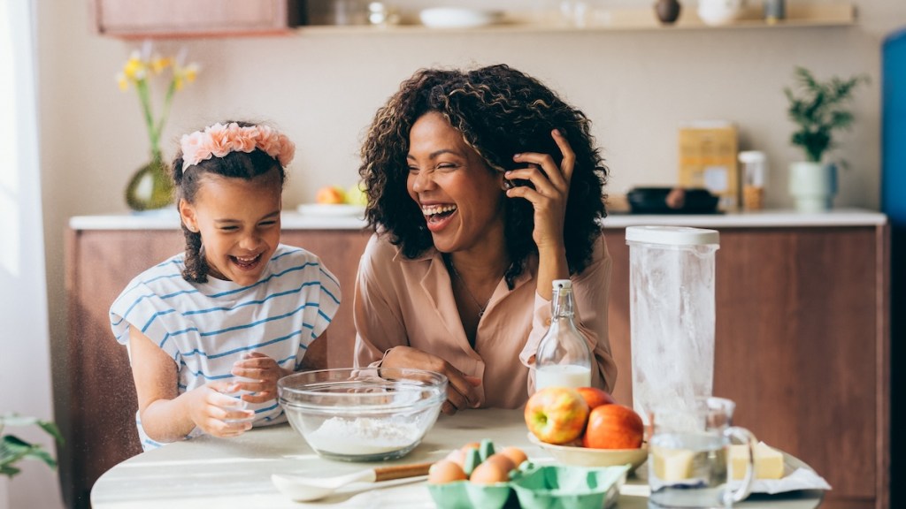 A woman laughs while preparing to cook in the kitchen with her young child