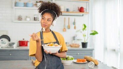 Young woman eating in her kitchen with headphones on
