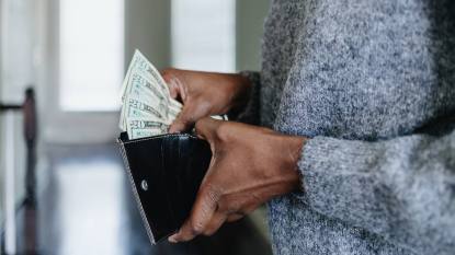 what are the richest zodiac signs: Close-up of unrecognizable black woman inserting twenty dollar bills into her wallet