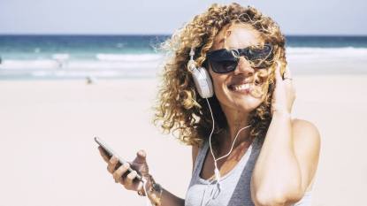 summer audiobooks: cheerful attractive beautiful caucasian middle age woman smiling at the beach in tropical place while listen music with the smart phone. people enjoying vacation and freedom from work holiday