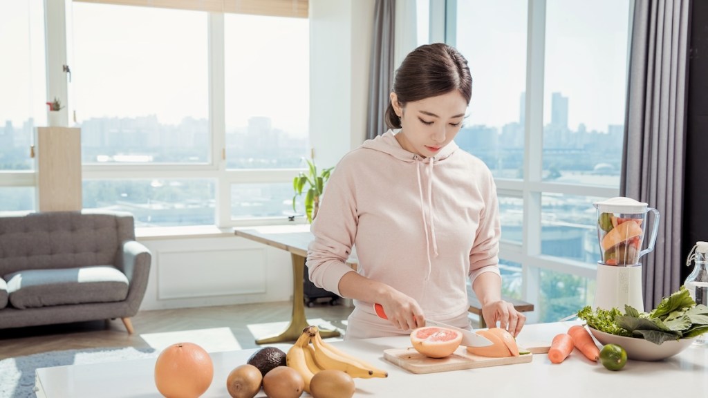 A young woman slices a grapefruit in the kitchen