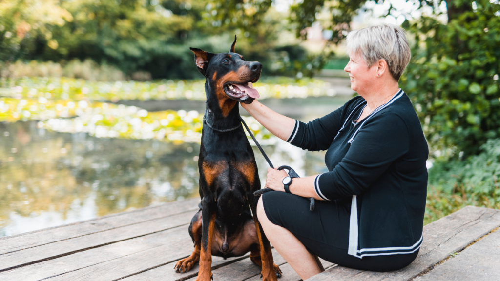 Woman sits by the lake with her doberman pinscher