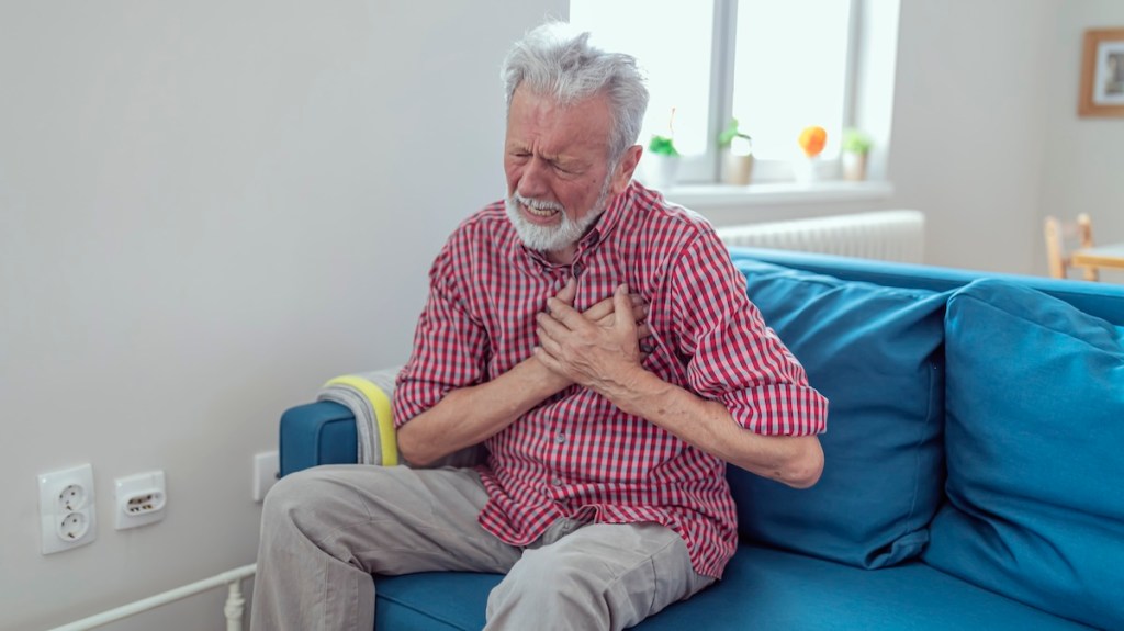 Man clutches chest while sitting on the couch