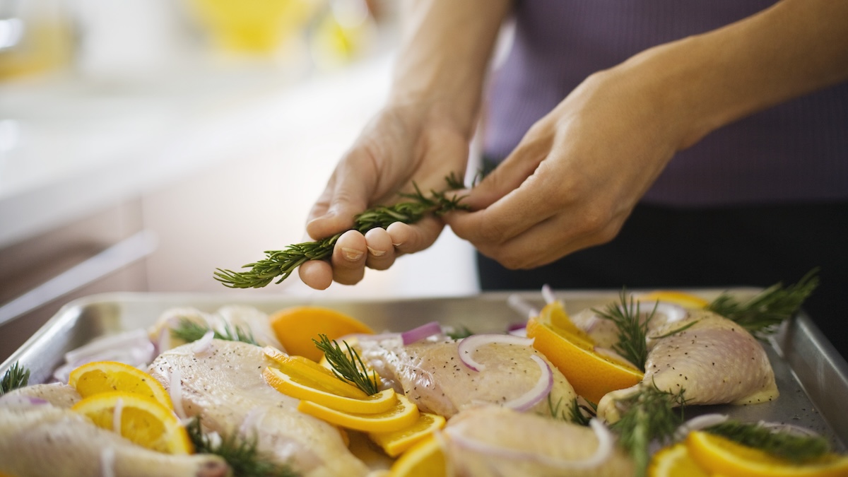 Person making a sheet pan meal with chicken, herbs and vegetables