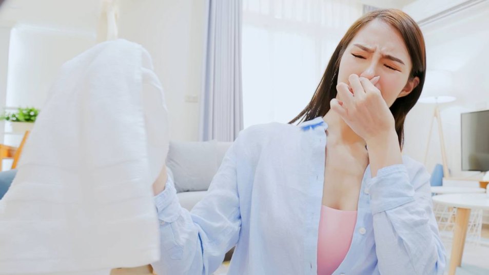 how to get rid of mildew smell in clothes: point of view from washing machine - asian brunette long hair woman frown with stinky clothes