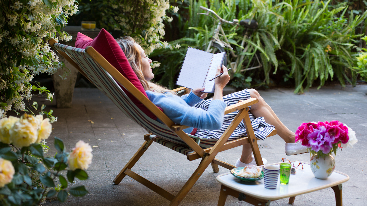 middle-aged woman reclines in a patio chair, taking in nature and writing in her intuition journal, as she learns how to tap into your intuition