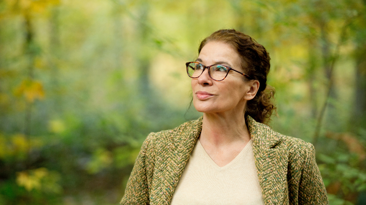 Women wearing eyeglasses looks off into space while surrounded by trees in a forest; she thinks about how to tap into your intuition.