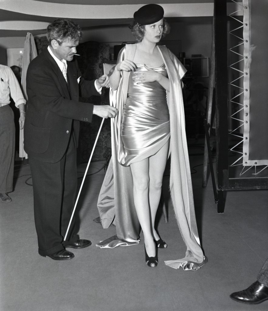 Yards of uncut satin were used to drape the figure of Lucille Ball (right) for sequences in which she portrays a model in the movie, ‘Beauty for the Asking.' Here , Director Glenn Tryon checks the folds in the drape arrangement before the final filming of scenes.