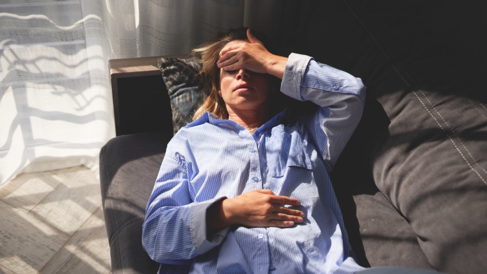 woman lies down covering her eyes with her hand as she suddenly gets an ocular migraine