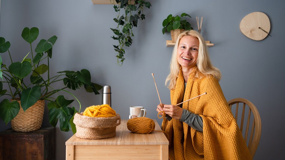 A woman knitting with golden yarn who's doing a craft from home job