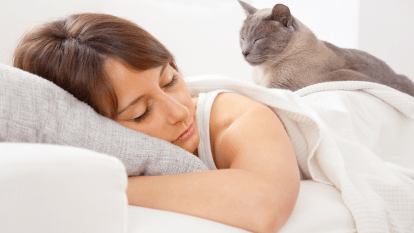 A woman sleeps while a cat sleeps on her back