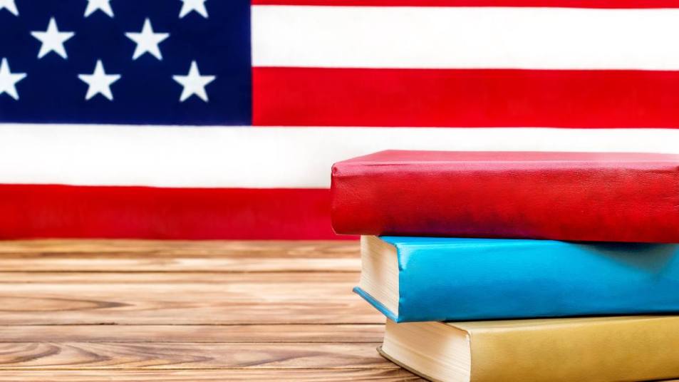 (revolutionary war books) Stack of books on the table against american flag. American education. Space for text.