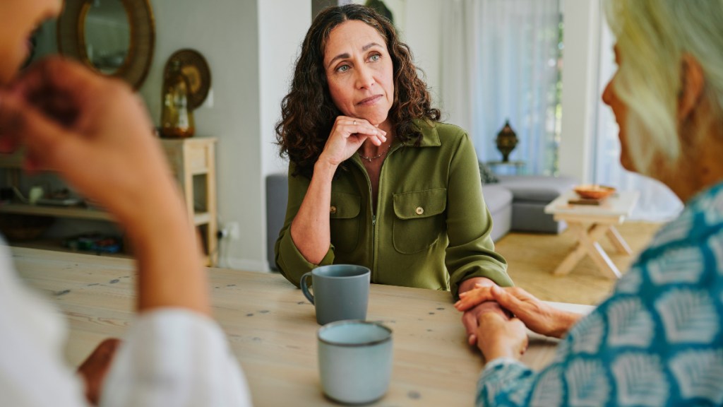 Mature woman holding her friend's hand in support as they talk about difficult emotions