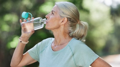 A mature woman drinking from a bottle of water outdoors on a sunny day