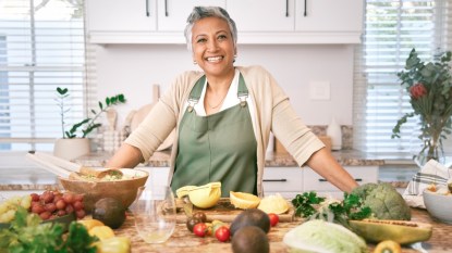 A mature woman in her kitchen with lots of fresh produce on the counter, avoiding common weight loss mistakes