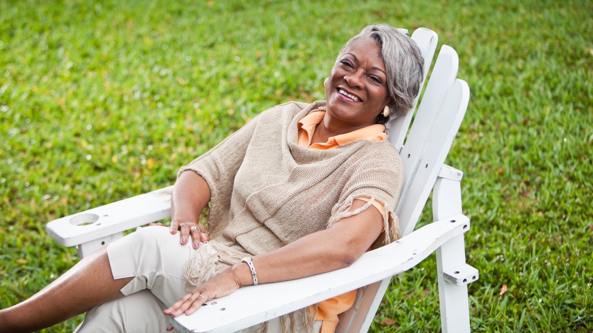 A mature Black woman relaxing in a white Adirondack chair in her yard after using home remedies for summer bothers