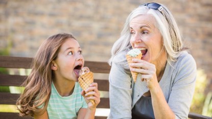 A mature woman sitting next to her granddaughter on a bench while eating ice cream and wondering what causes brain freeze