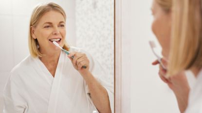 mature woman with receding gums brushing teeth in front of mirror