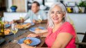 A mature woman in a pink top sitting at a dinner table, choosing what foods to avoid while taking semaglutide