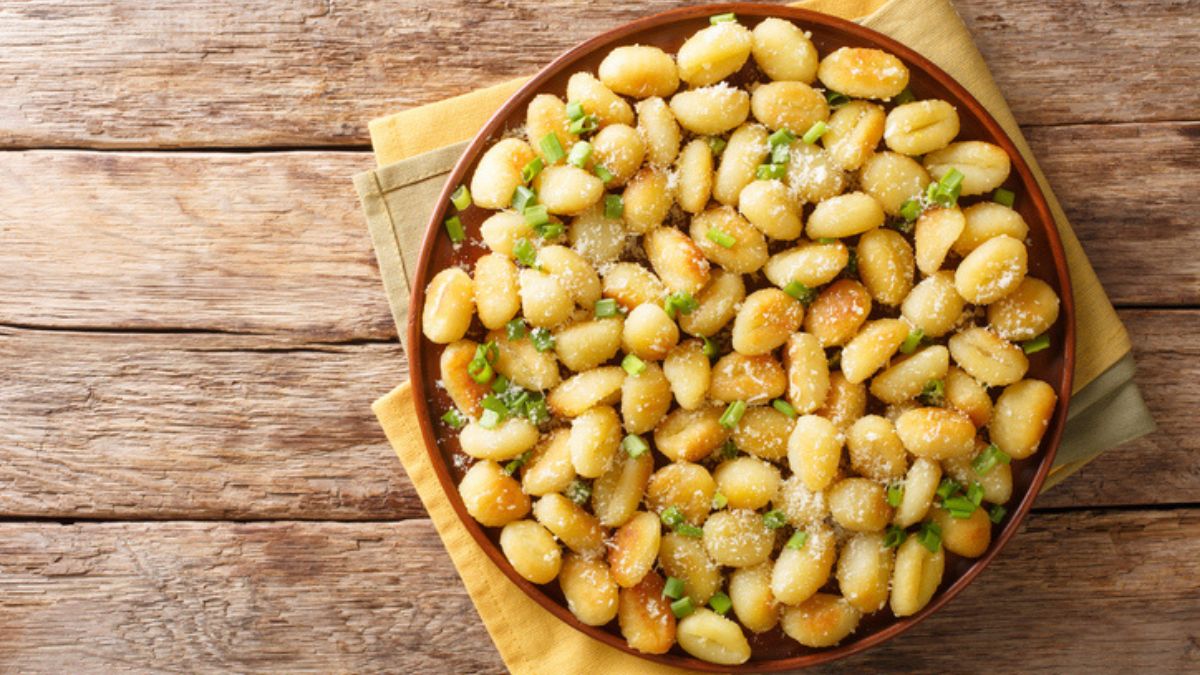 bowl of pan-fried gnocchi with parmesan cheese and fresh herbs against wooden background