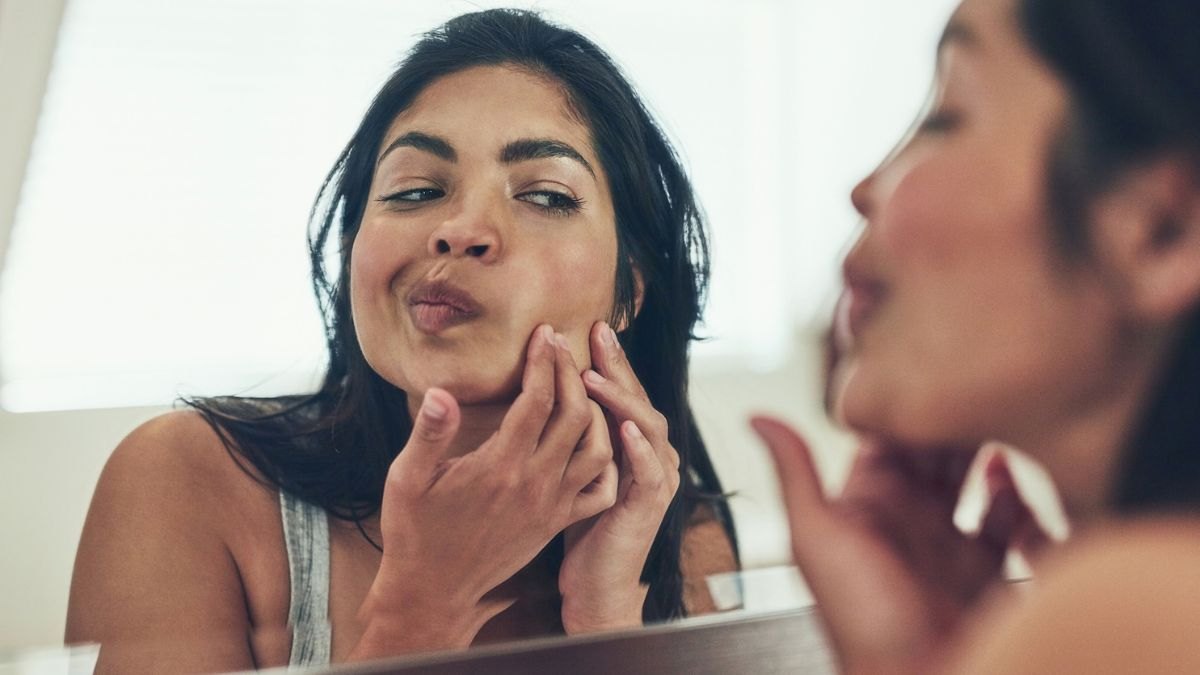 A woman looking at a her skin in the mirror before applying an invisible pimple patch