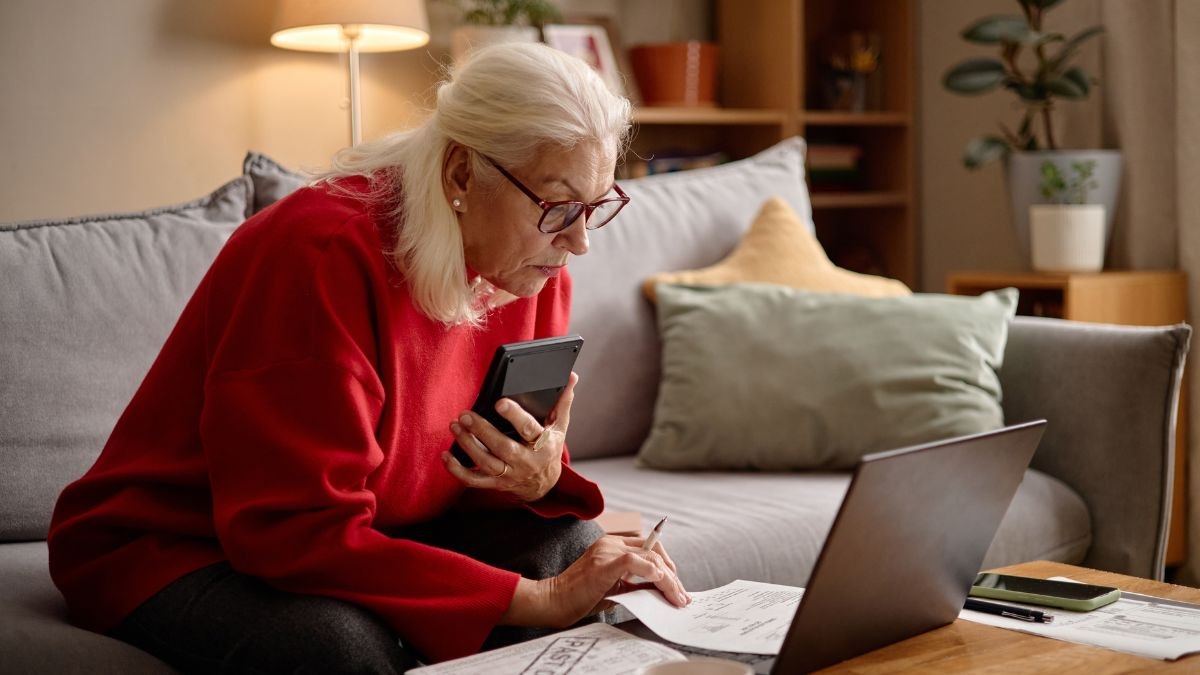 Senior Woman Reviewing Bills While Using Smartphone and Laptop