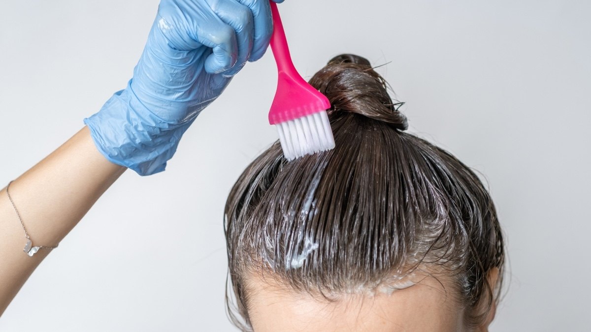 Close-up of a woman applying at-home hair color with gloves and a brush