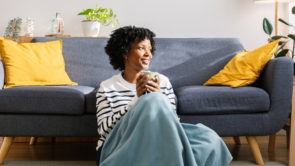 A woman sitting with a warm blanket and cup of tea to help treat her seasonal affective disorder